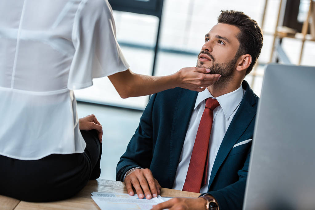cropped view of woman touching face of handsome bearded businessman while sitting on table  - Photo, Image
