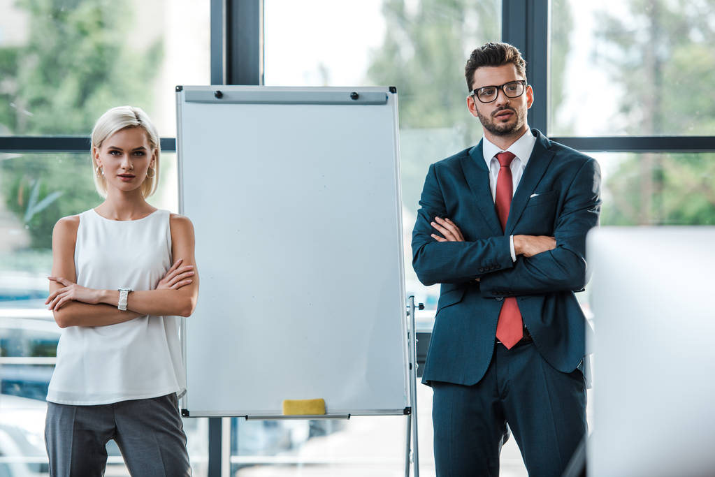 handsome businessman in glasses and beautiful blonde businesswoman standing with crossed arms in office  - Photo, Image
