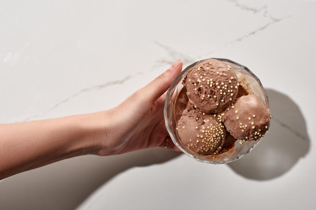 részleges kilátás a nő gazdaság finom csokoládé fagylalt tálban márvány szürke háttér - Fotó, kép
