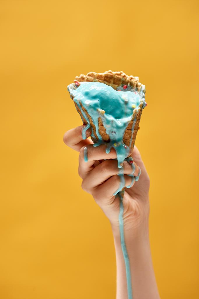 黄色に分離されたサクサクのワッフルコーンで溶けた青いアイスクリームを持つ女性のトリミングされたビュー - 写真・画像