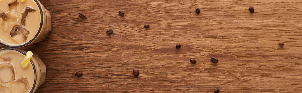 木製のテーブルの上のコーヒー粒の近くのメガネでアイスコーヒーのトップビュー、パノラマショット - 写真・画像