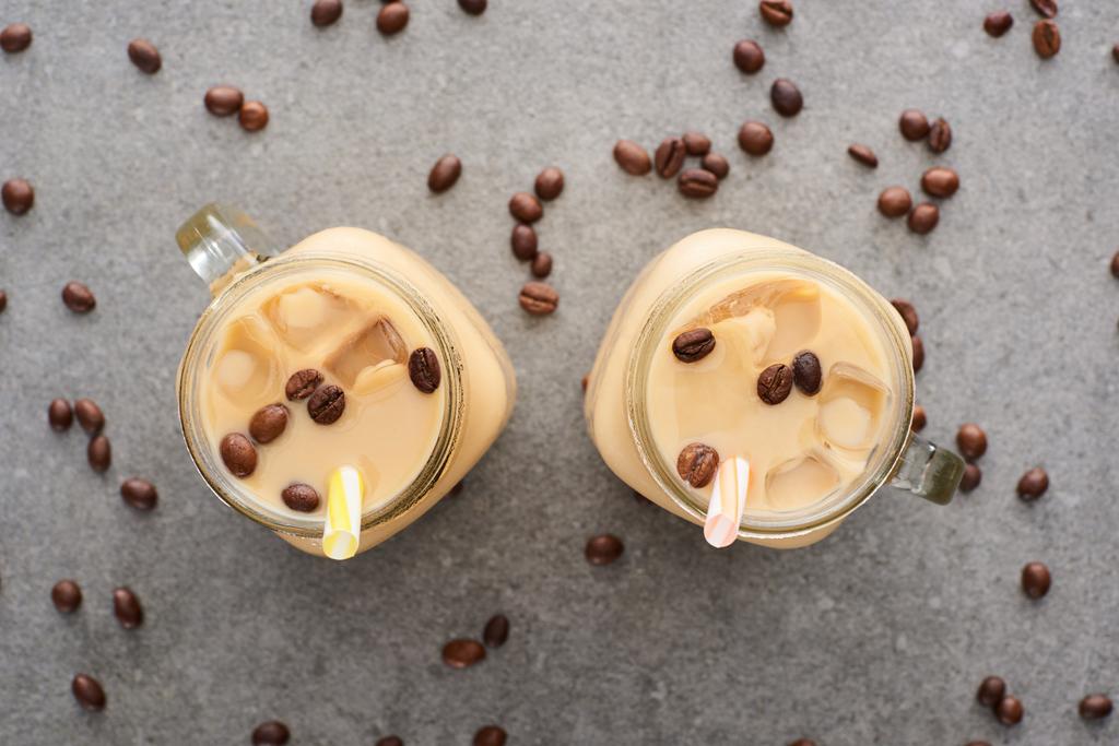 top view of ice coffee in glass jars with straws and coffee grains on grey background - Photo, Image