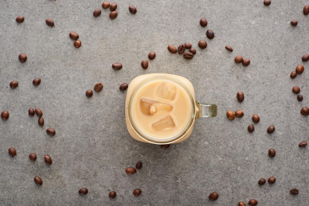 Draufsicht auf köstlichen Eiskaffee im Glas in der Nähe von Kaffeekörnern auf grauem Hintergrund - Foto, Bild