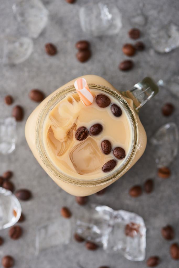 selektiver Fokus von Eiskaffee im Glas mit Stroh in der Nähe von Kaffeekörnern und Eiswürfeln auf grauem Hintergrund - Foto, Bild