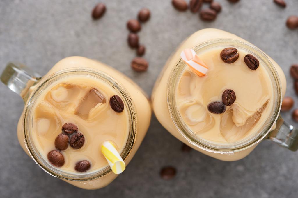 Top uitzicht van smakelijke ijskoffie met rietjes en koffiebonen op grijze achtergrond - Foto, afbeelding