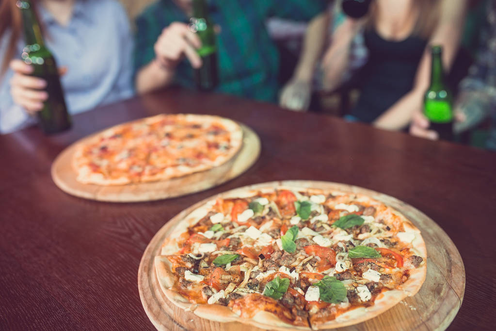 Arkadaşlar bir barda bir içki sahip, onlar bira ve pizza ile ahşap bir masada oturuyor - Fotoğraf, Görsel