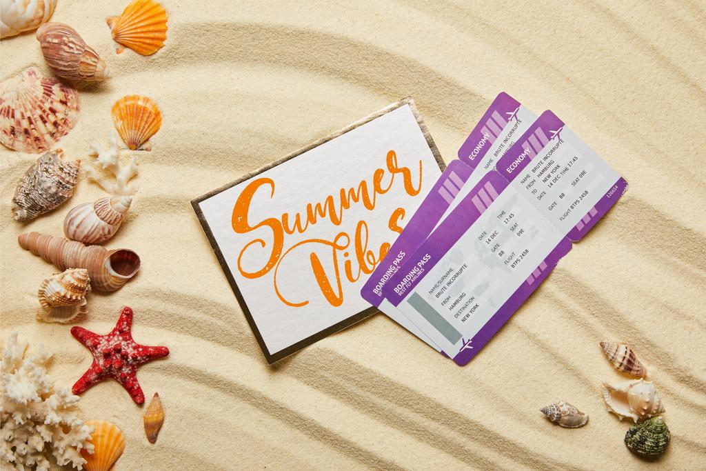 vista superior de la tarjeta con vibraciones de verano dejando cerca de boletos aéreos y conchas marinas en la playa de arena
 - Foto, Imagen