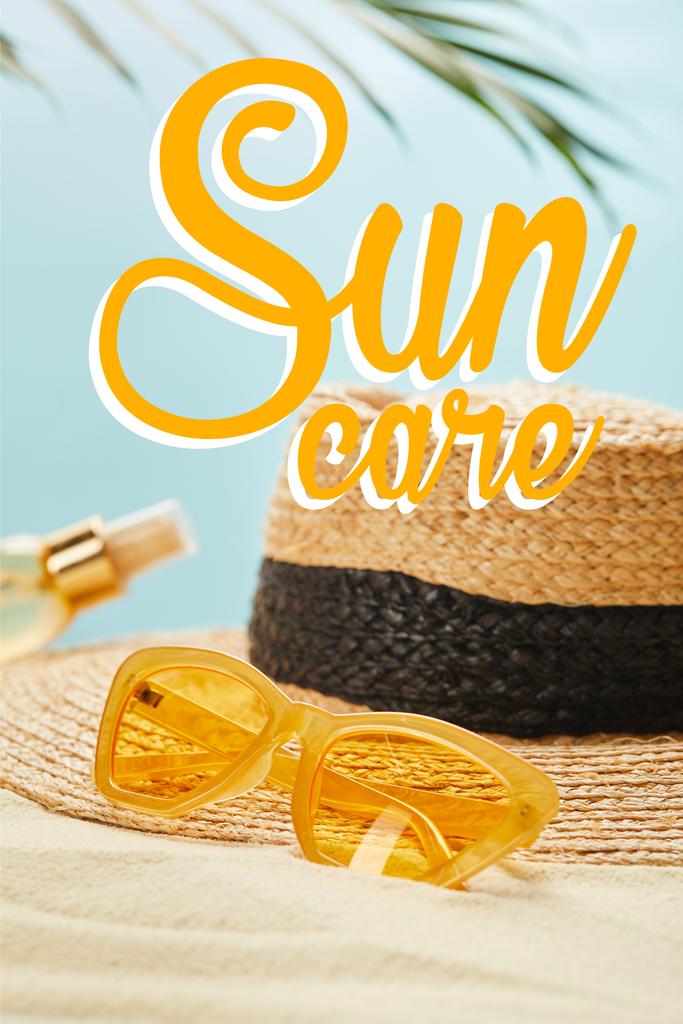 gafas de sol cerca de sombrero de paja y botella con aceite bronceador en la playa de arena aislada en azul con ilustración de cuidado del sol
 - Foto, imagen