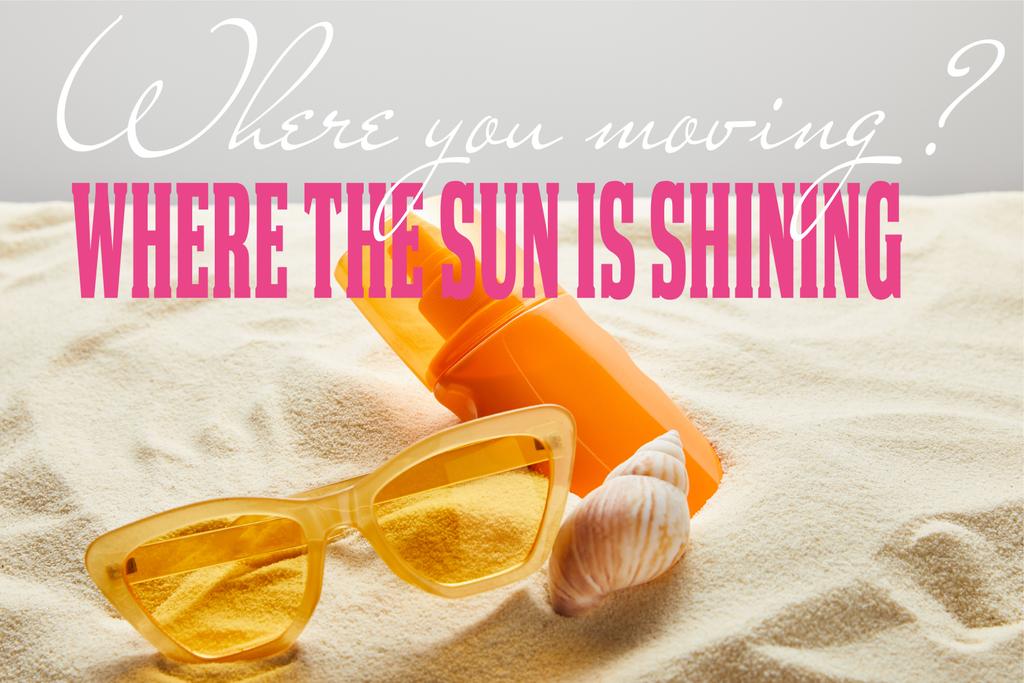 κίτρινα κομψά γυαλιά ηλίου και αντηλιακό σε πορτοκαλί μπουκάλι στην άμμο με κοχύλι σε γκρίζο φόντο με το σημείο που κινείστε ερώτηση και όπου ο ήλιος λάμπει απάντηση - Φωτογραφία, εικόνα