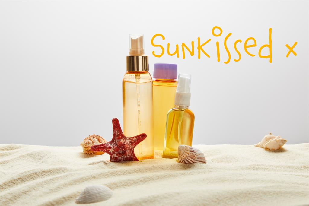 бутылки с солнцезащитными средствами на песке с морской звездой на сером фоне с надписью, поцелованной солнцем
 - Фото, изображение