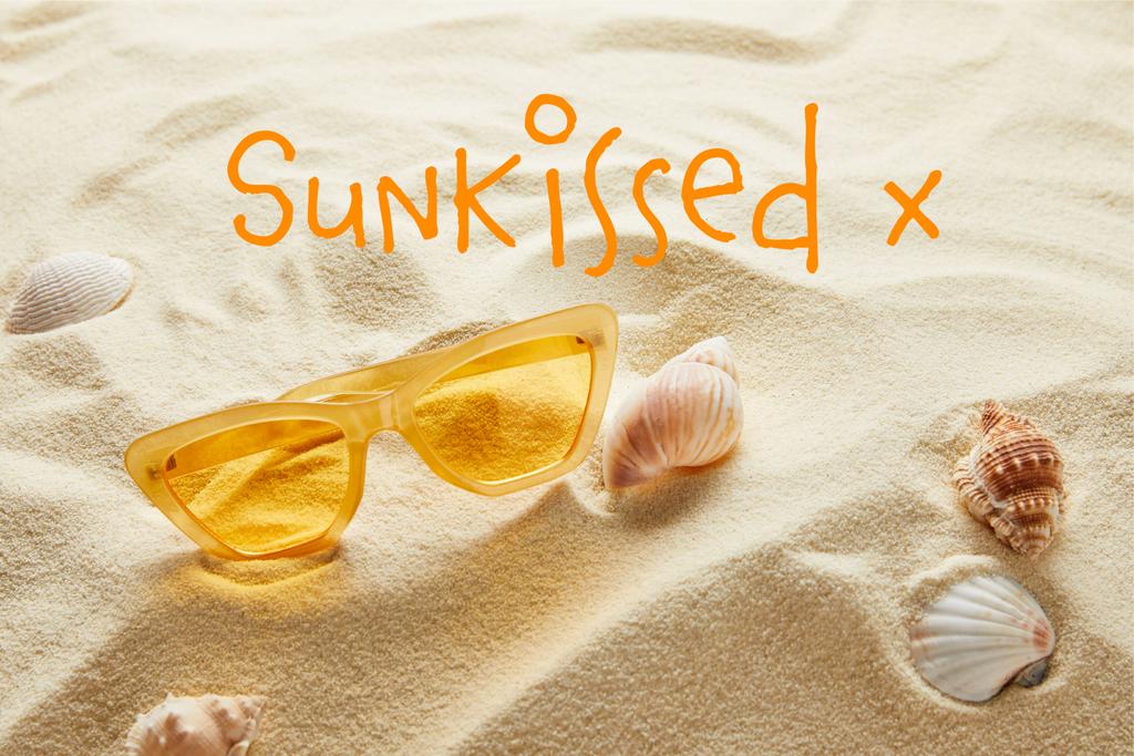 żółte stylowe okulary przeciwsłoneczne na piasku z muszli i pocałowanymi słońcem napisem - Zdjęcie, obraz