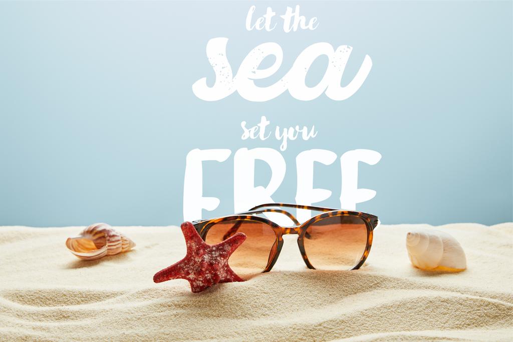 brązowe stylowe okulary przeciwsłoneczne na piasku z muszli i rozgwiazdy na niebieskim tle z niech morze zestaw ci wolne napis - Zdjęcie, obraz
