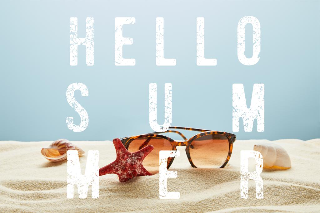 brown stylish sunglasses on sand with seashells and starfish on blue background with hello summer lettering - Photo, Image