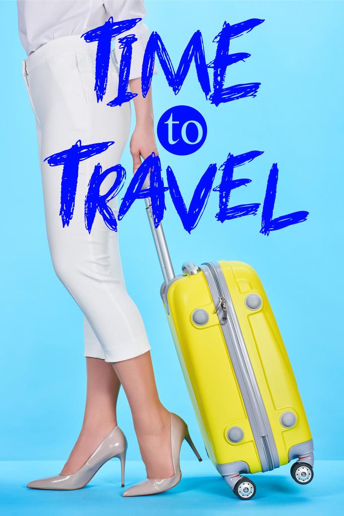 vista recortada de la mujer que sostiene la manija de la bolsa de viaje amarilla sobre fondo azul con el tiempo para viajar ilustración
  - Foto, Imagen