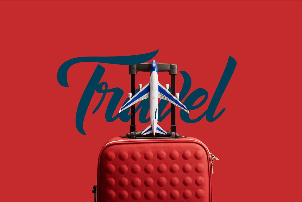 κόκκινη πολύχρωμη τσάντα ταξιδιού με αεροπλάνο μοντέλο απομονωμένο σε κόκκινο με ταξιδιωτική απεικόνιση - Φωτογραφία, εικόνα