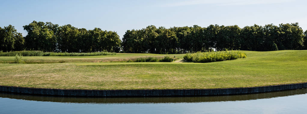 池と青空の近くの緑の草や木のパノラマショット  - 写真・画像