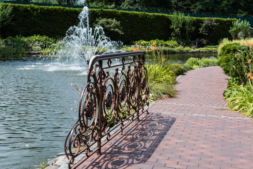 selective focus of metallic fence on bridge near lake with fountain  - Photo, Image