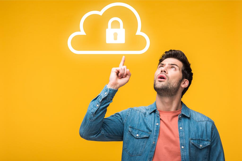 confused handsome man pointing with finger at internet security icons isolated on yellow - Photo, Image