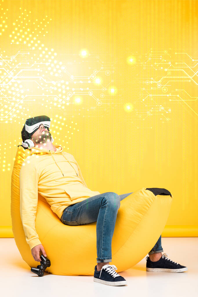 KYIV, UKRAINE - 12 AVRIL : homme dormant sur une chaise de sac de haricots avec joystick en réalité virtuelle casque sur jaune avec illustration du cyberespace
 - Photo, image