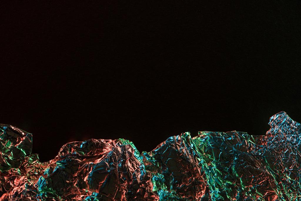 Κορυφαία όψη του τσαλακωμένο φύλλο με πολύχρωμη αντανάκλαση φωτισμού στο σκοτάδι που απομονώνεται σε μαύρο με χώρο αντιγραφής - Φωτογραφία, εικόνα