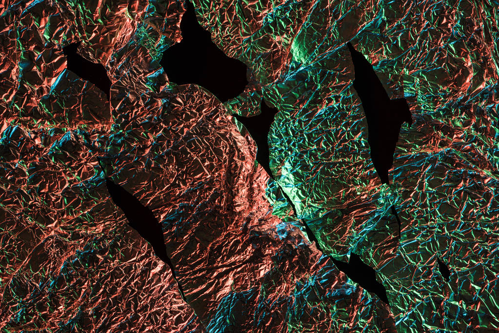 Κορυφαία όψη του σχισμένο τσαλακωμένο αλουμινόχαρτο με πολύχρωμη αντανάκλαση φωτισμού στο σκοτάδι που απομονώνεται σε μαύρο - Φωτογραφία, εικόνα