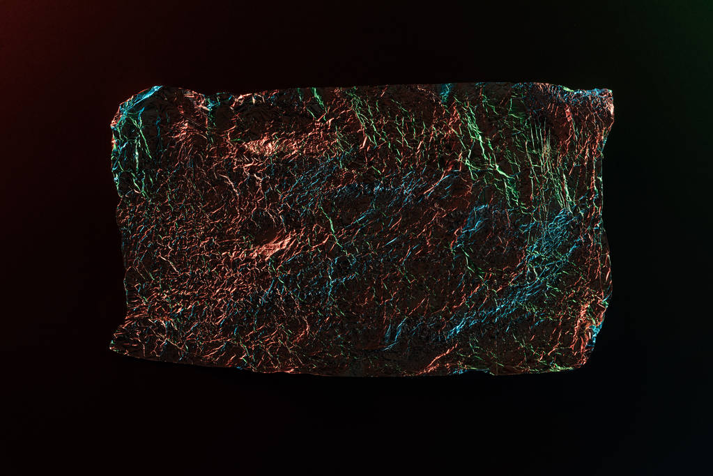 Κορυφαία όψη του γυαλιστερού τσαλακωμένων φύλλων με πολύχρωμη αντανάκλαση φωτισμού που απομονώνεται σε μαύρο - Φωτογραφία, εικόνα