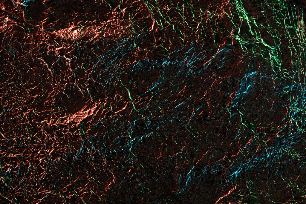 κορυφή όψη του αργύρου τσαλακωμένο φύλλο με πολύχρωμο φωτισμό στο σκοτάδι - Φωτογραφία, εικόνα