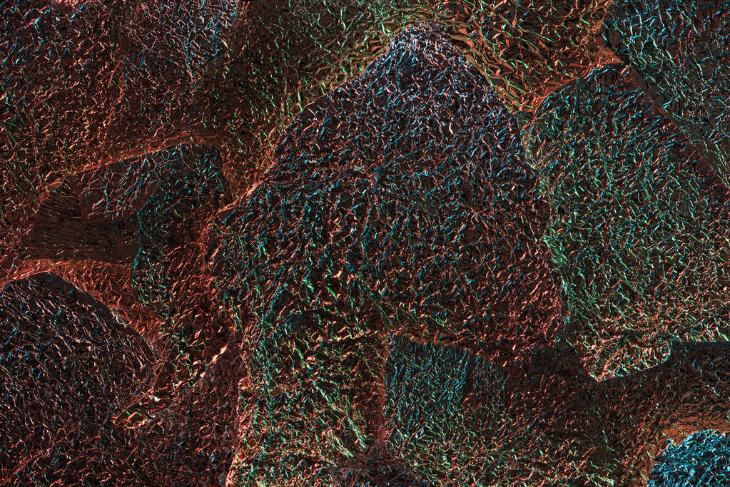 abstracte achtergrond van glanzend getextureerde ragged folie met kleurrijke verlichting - Foto, afbeelding
