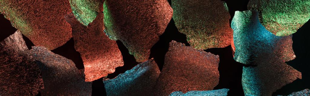panoramische foto van abstracte achtergrond van gescheurde folie met kleurrijke verlichting geïsoleerd op zwart - Foto, afbeelding