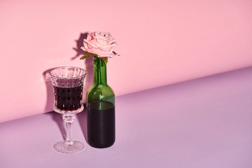 γυαλί και φιάλη με τριαντάφυλλο σε φωτεινό και πολύχρωμο φόντο με χώρο αντιγραφής  - Φωτογραφία, εικόνα