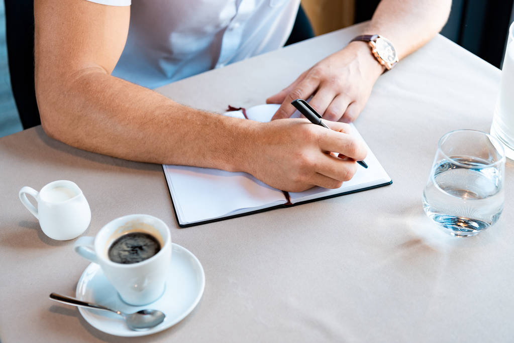 osittainen näkymä mies kirjoittaa oppikirjassa istuessaan kahvilassa
 - Valokuva, kuva
