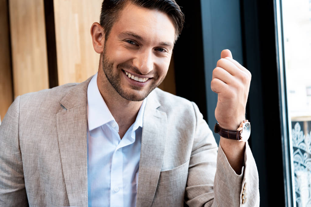 sonriente hombre de negocios en reloj de pulsera mirando a la cámara en la cafetería
 - Foto, Imagen
