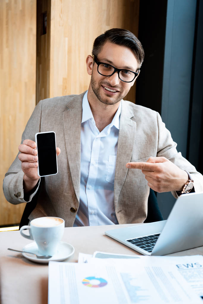 бизнесмен указывает пальцем на смартфон с пустым экраном в кафе
 - Фото, изображение