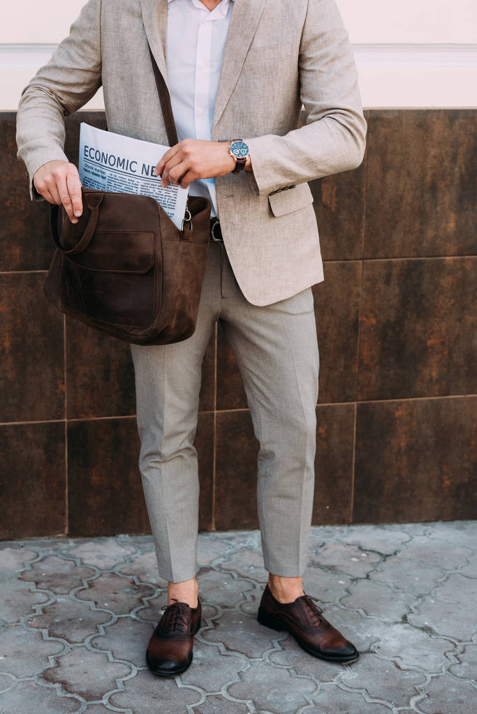 路上に立つバッグに新聞を持つ腕時計のビジネスマンのトリミングビュー - 写真・画像
