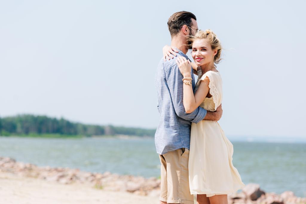 hymyilevä blondi nainen halaus parrakas poikaystävä rannalla
 - Valokuva, kuva