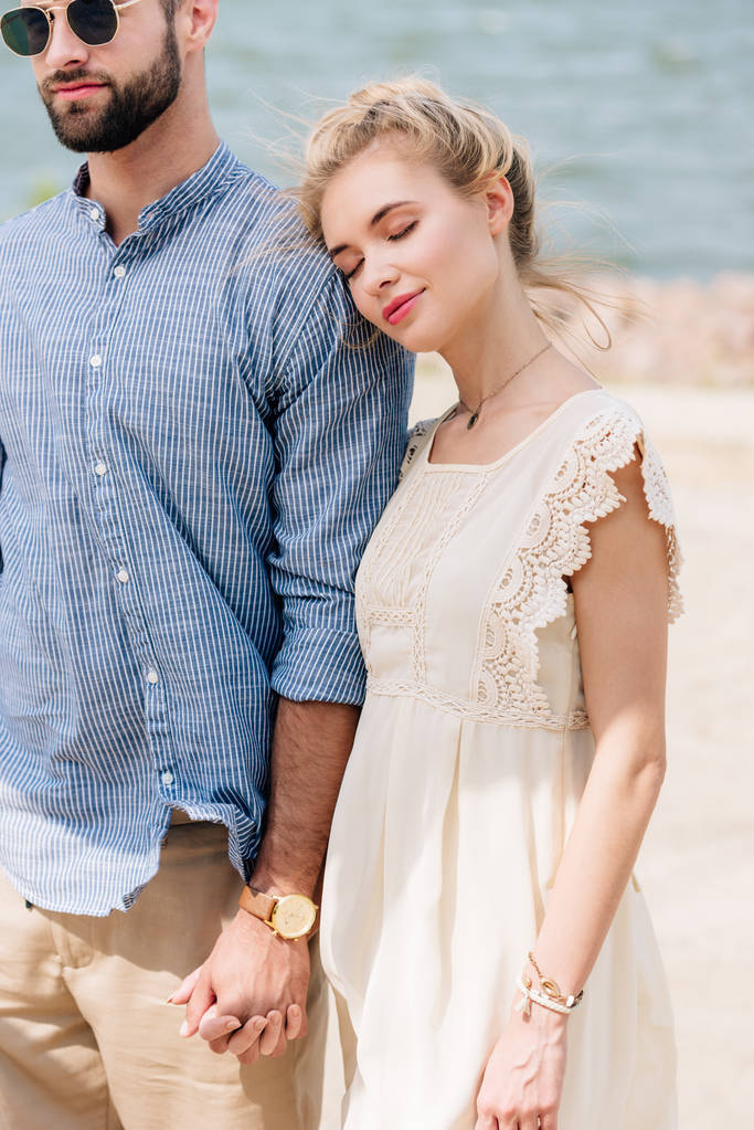 blond meisje met gesloten ogen leunend op vriendje schouder op strand - Foto, afbeelding