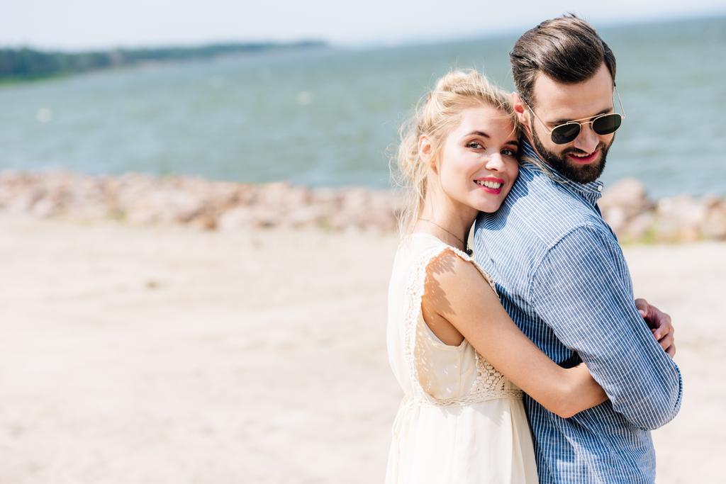 felice donna bionda abbracciare barbuto sorridente fidanzato in spiaggia
 - Foto, immagini