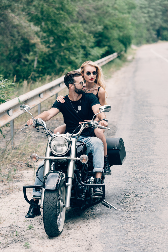 young couple of bikers on black motorcycle on road near green forest - Photo, Image