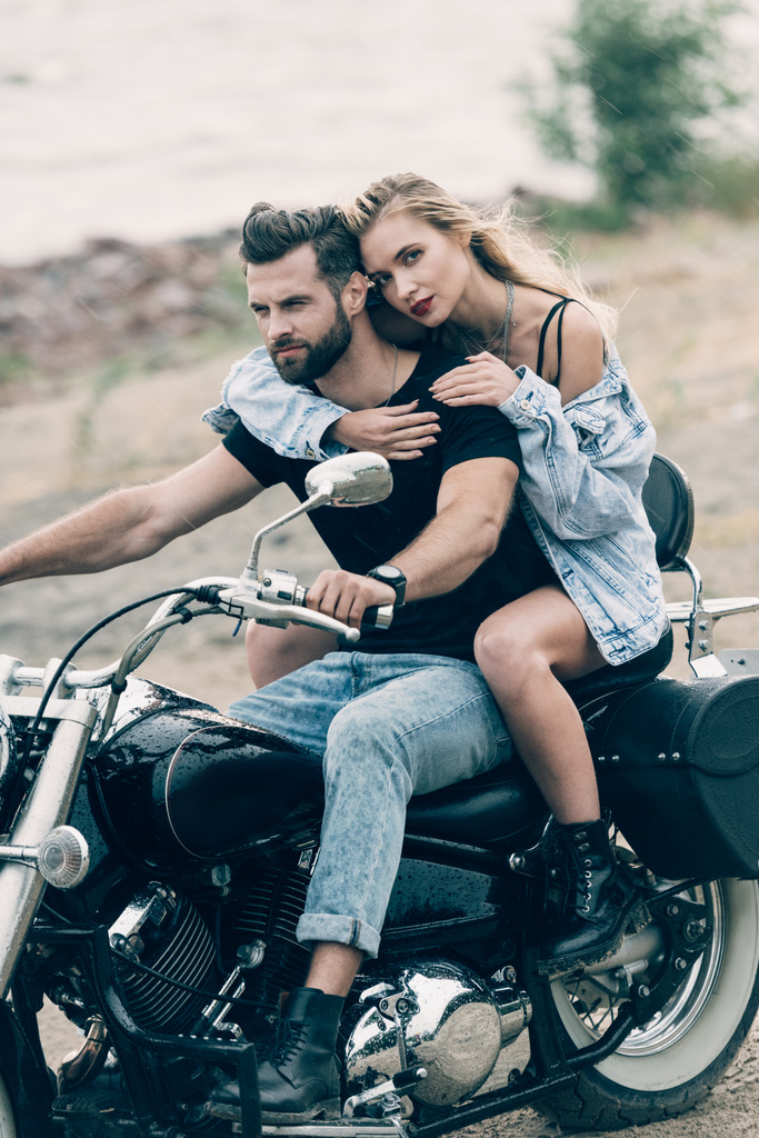 jovem casal de motociclistas abraçando na motocicleta preta na praia de areia
 - Foto, Imagem