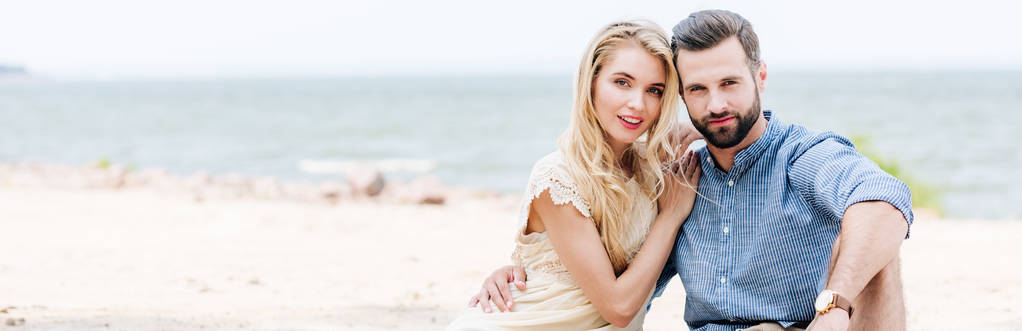 krásný mladý pár sedící na pláži blízko moře, panoramatický záběr - Fotografie, Obrázek