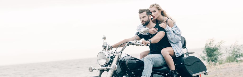 giovane coppia amorevole di motociclisti seduti sulla moto nera sulla spiaggia vicino al fiume, colpo panoramico
 - Foto, immagini