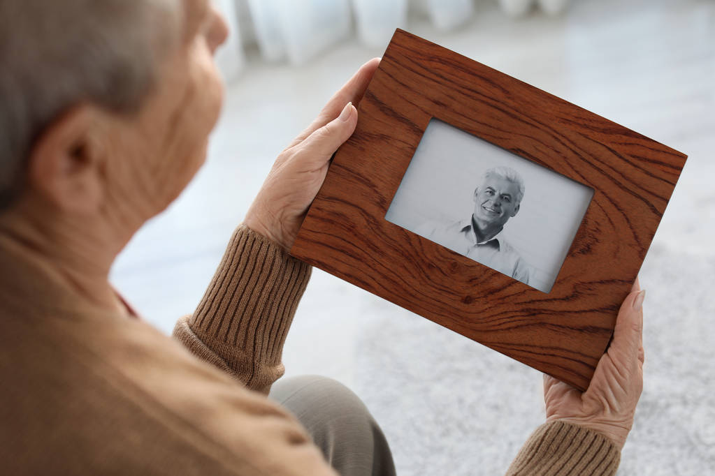 Ηλικιωμένη γυναίκα με κορνίζα φωτογραφία του γιου της στο σπίτι - Φωτογραφία, εικόνα