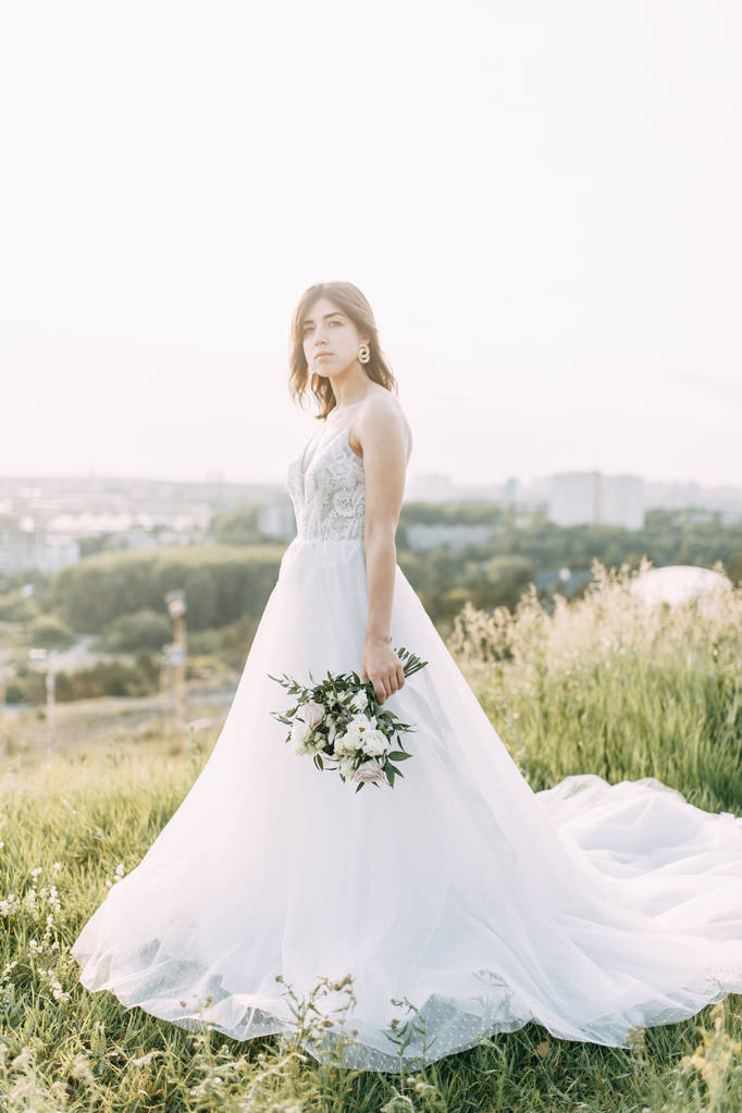 Νύφη με μακρύ φόρεμα στη φύση με το ηλιοβασίλεμα. Ένας κομψός γάμος στο Ευρωπαϊκό στυλ της καλών τεχνών.  - Φωτογραφία, εικόνα