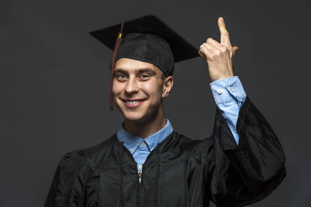 帽子をかぶった黒い卒業ガウンを着た大学院生の成人男子学生の肖像 - 写真・画像