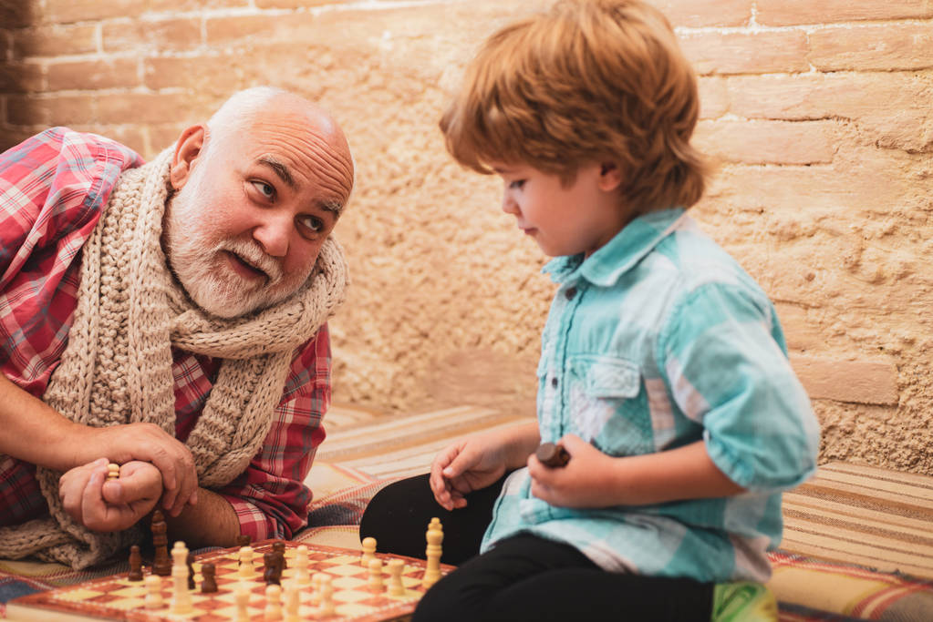 Starší muž uvažuje o dalším pohybu v šachu. Děda a vnuk hrají šachy. Dědeček hrál šachy se svým vnukem. - Fotografie, Obrázek