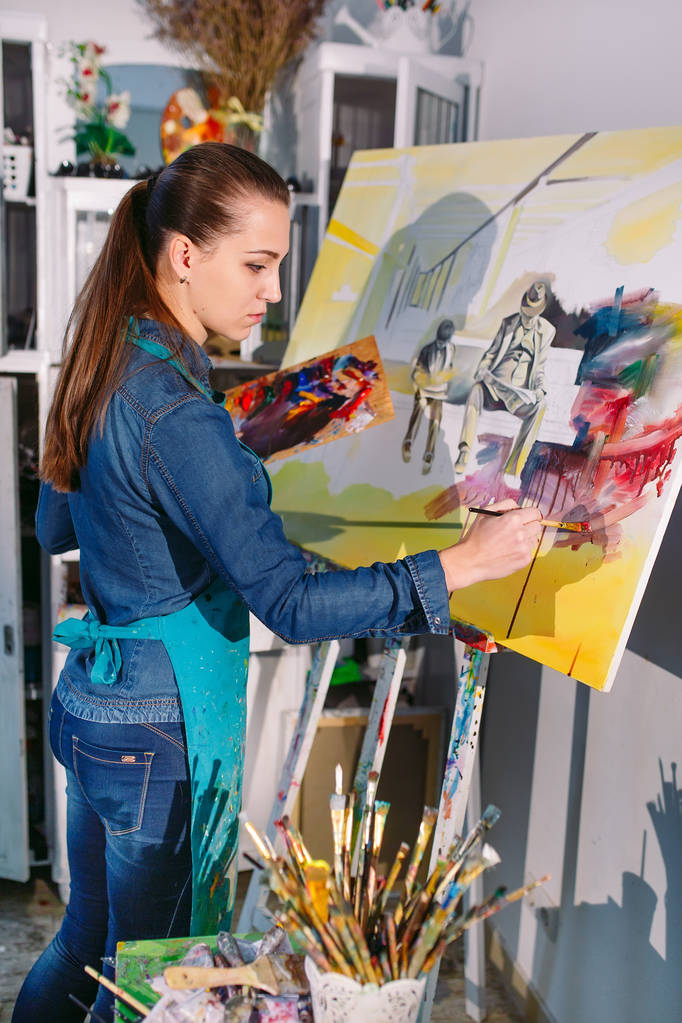 Όμορφο κορίτσι σε ένα στούντιο ζωγραφικής ζωγραφίζει μια εικόνα. - Φωτογραφία, εικόνα