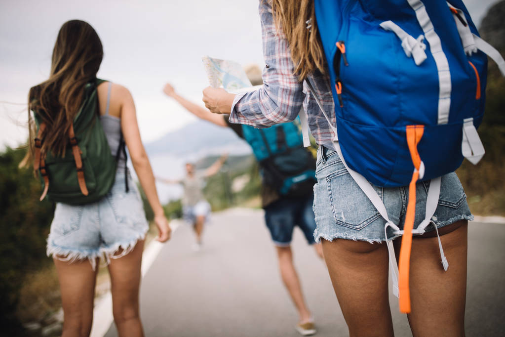 Arkadaşlarla yürüyüş yapmak çok eğlenceli. Sırt çantalı bir grup genç yol kenarında birlikte yürüyor. - Fotoğraf, Görsel