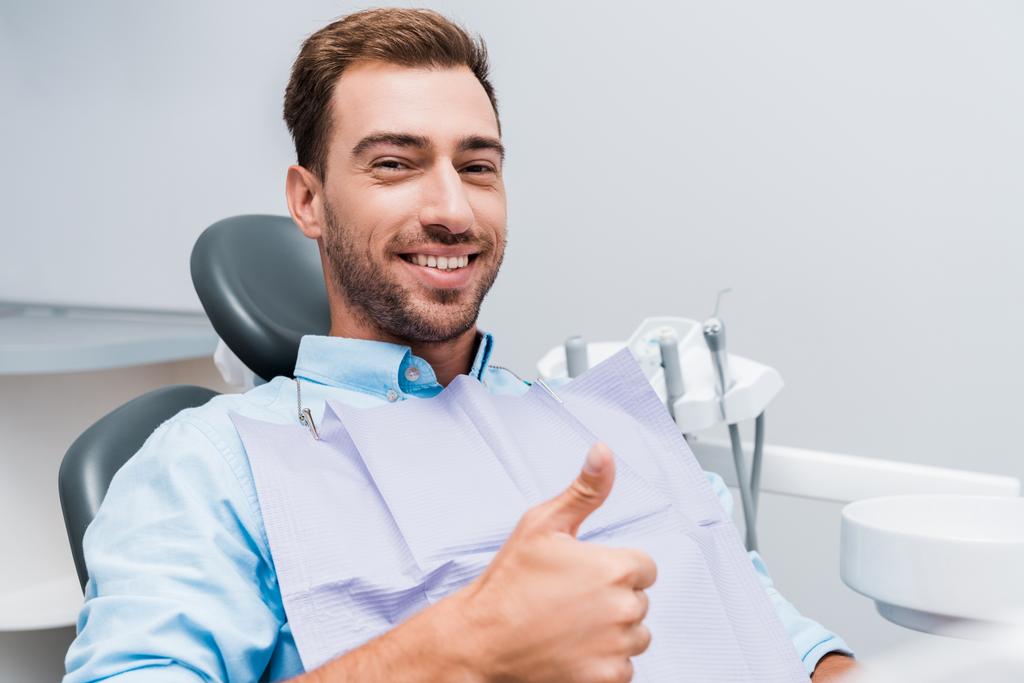 glücklicher bärtiger Mann lächelt und zeigt Daumen hoch in Zahnklinik  - Foto, Bild
