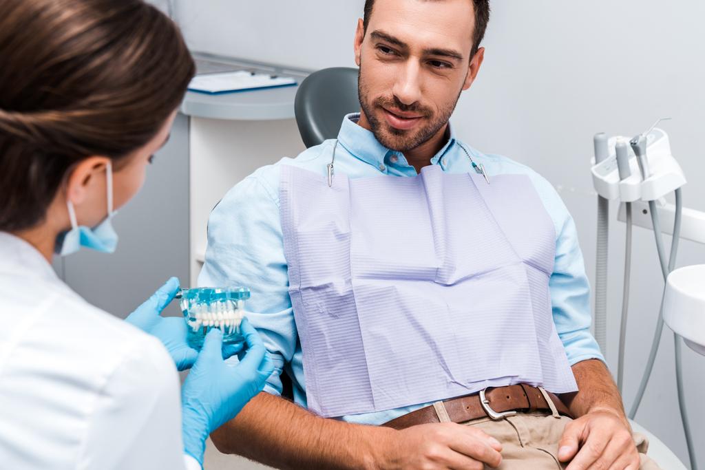 klinikte diş modeli tutan diş hekimi bakarak yakışıklı adamın seçici odak  - Fotoğraf, Görsel