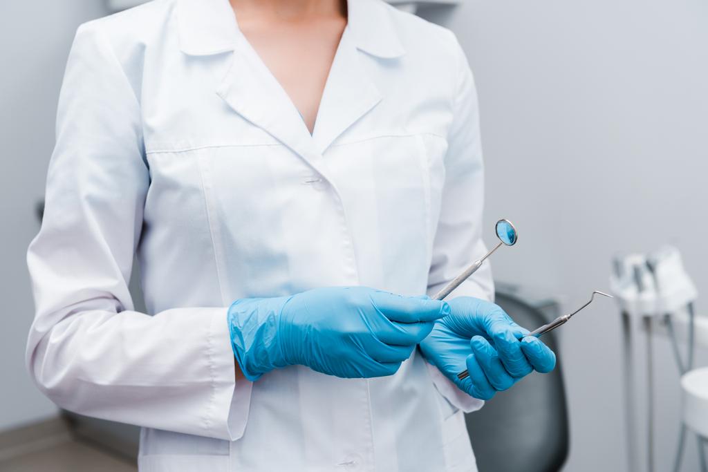 vue recadrée du dentiste en gants de latex bleu tenant des instruments médicaux en acier inoxydable
  - Photo, image